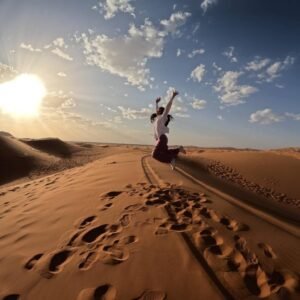 Woman jumping joyfully on a sand dune at sunset during a 3 Days Tour from Marrakech to Merzouga