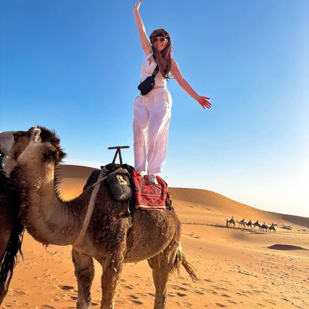 Woman standing confidently on a camel during a desert tour arranged by the Best Morocco Tours Agency.