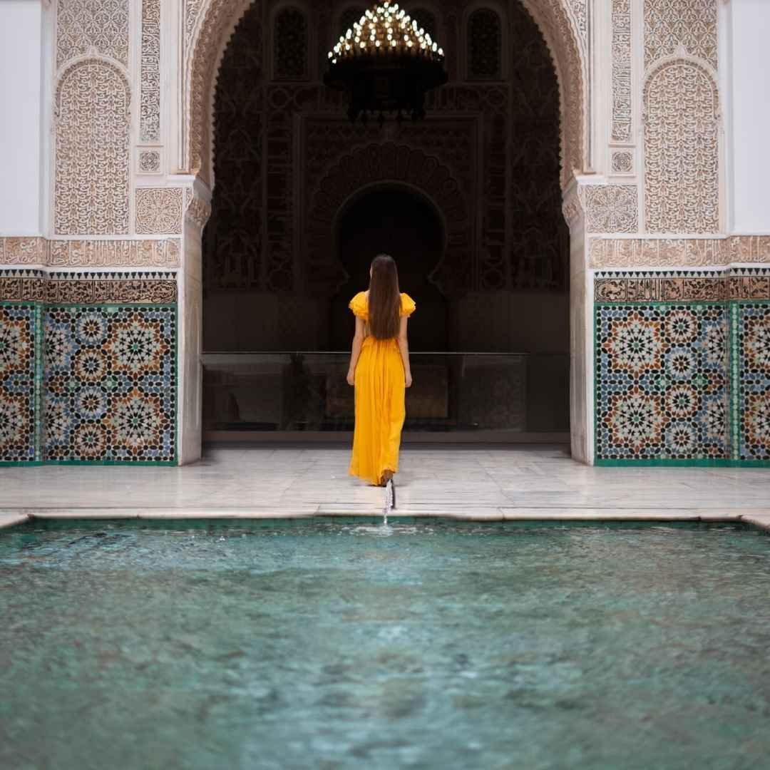 Woman in yellow dress walking toward a Moroccan palace interior with pool, curated by Best Morocco Tours Agency Go Morocco Ogle.